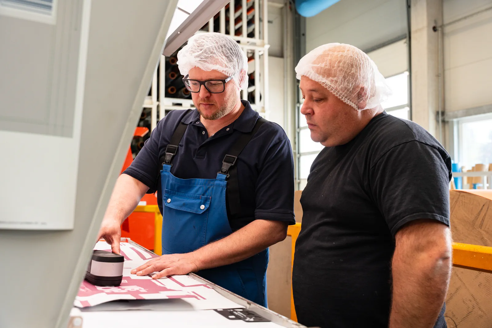 Zwei Flexopack-Mitarbeiter prüfen einen frisch bedruckten Etikettenbogen